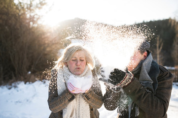 Beautiful senior couple blowing snow in sunny winter nature