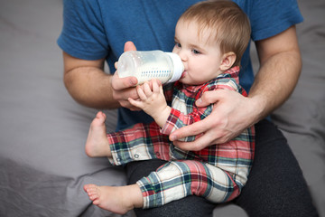 Adorable baby drinking milk from bottle in father hands
