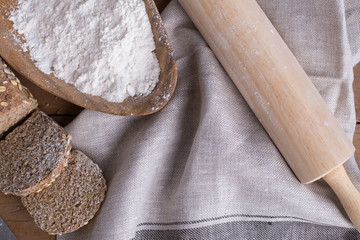 Whole grain wheat bread set on nice fabric brown background decorated with flour bowl and a bakery wooden roller.