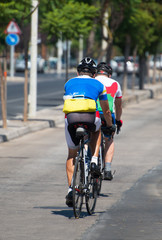 Two sportsmen riding on bicycles around the city.