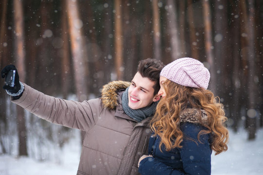 happy couple taking picture with smartphone selfie stick on over winter background