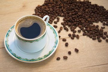 Stimulating cup of black coffee on a wooden table with coffee grains