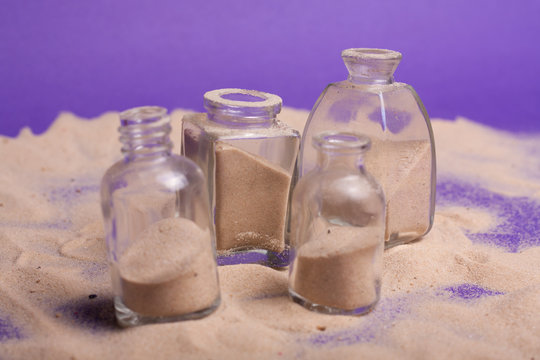 garrafas pequenas com areia em fundo roxo