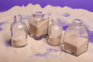 garrafas pequenas com areia em fundo roxo