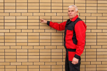 Fototapeta na wymiar Builder in black and red jumpsuit hand shows on a brick wall.Pla