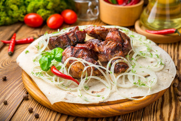 Pieces of meat with onions on skewers kebab . Serve with sauce, tomatoes and arugula. top view