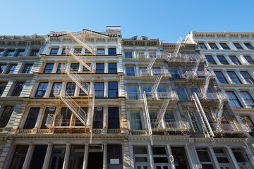 Typical building facades with fire escape stairs, sunny day in New York