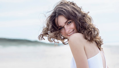 Naklejka premium Szczęśliwa kobieta na plaży. Portret pięknej dziewczyny zbliżenie, wiatr fruwające włosy. Wiosna portret na plaży. Młoda ładna dziewczyna. Młody uśmiechnięty kobieta portret outdoors. Zamknij portret.