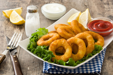 Fried calamari rings with lettuce and ketchup on wooden background
