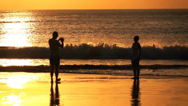 Man taking photo of his girlfriend on beach during sunset, super slow motion 240fps

