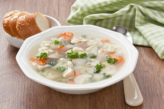 Soup with chicken, cauliflower, vegetable and bread in white plate / Vegetable soup with chicken, cauliflower, carrot, potato, green peas, parsley and slice white bread in plate on wooden background