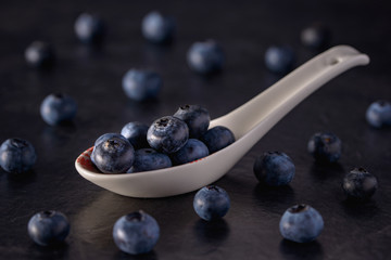 Spoon with fresh blueberry on black background, selective focus