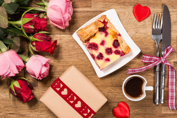 Raspberry cake on white plate, red hearts, coffee and roses on wooden background. Valentines Day background