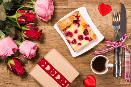 Raspberry cake on white plate, red hearts, coffee and roses on wooden background. Valentines Day background