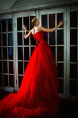 Beautiful girl in long red dress and in royal crown standing near retro fireplace door with stained-glass windows