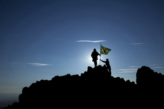 Two soldiers raise the Brazilian flag on a mountain top