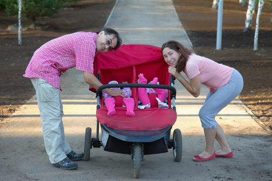 Happy Parents With Baby Buggy And Twin Daughters In It Walking I