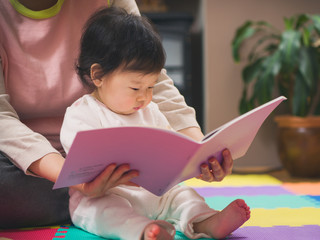 Asian baby girl reading book with mom © M-image