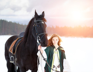 Fototapeta premium Young girl in white dress with black thoroughbred horse on winter field. Historical equine background