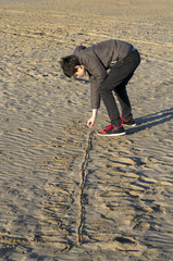 Boy playing with sand on the beach. Teenager on Mediterranean seacoast of Valencia, Spain during winter.