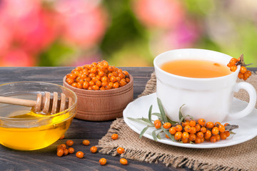 Tea of sea-buckthorn berries with honey on wooden table blurred garden background