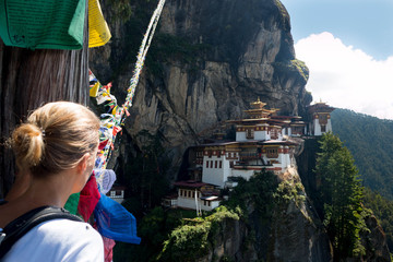 Bhutan Taktshang monastery Tigers Nest temple blonde woman looking the landmark on a mountain with prayer flags - 132763398