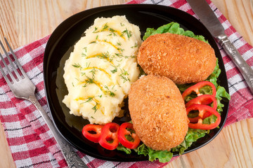 two fried breaded cutlet with mashed potatoes and lettuce on a black plate  wooden background