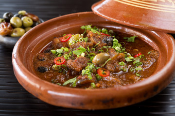 Sambal chicken tajine served with olives, in a rustic beautiful tagine pot, photographed with a shallow depth of filed. World cuisine.