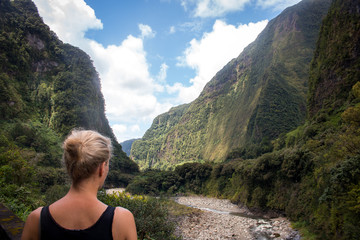Ile de la Reunion blonde woman looking into a green mountain canyon and riverbed landscape - 132765903
