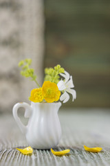 Ranunculus bouquet in miniature, diminutive jug. Macro close-up photo with soft focus, bouquet of buttercup flowers. Rustic background