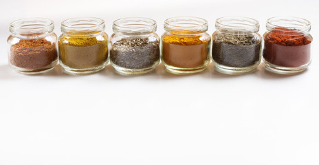 Spices in glass jars, turmeric, thyme, oregano, paprika, curry, for pilaf. Isolated on white.