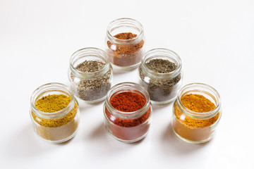 Spices in glass jars, turmeric, thyme, oregano, paprika, curry, for pilaf. Isolated on white.