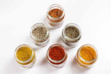 Spices in glass jars, turmeric, thyme, oregano, paprika, curry, for pilaf. Isolated on white.