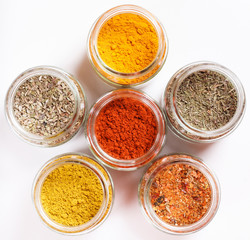 Spices in glass jars, turmeric, thyme, oregano, paprika, curry, for pilaf. Isolated on white.