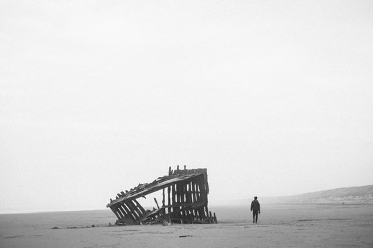 A man walks past a shipwreck on the beach at Fort Stevens State Park in Oregon