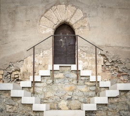 an ancient stone made wall with a rusty metallic door and a staircase