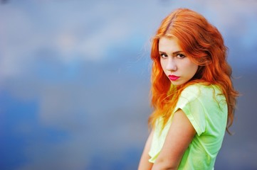 Portrait of a very beautiful brown eyed girls with bright red hair in a light green dress on a background of lake