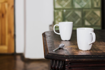 Two White Mugs with Silver Spoon on Wooden Brown Table. 