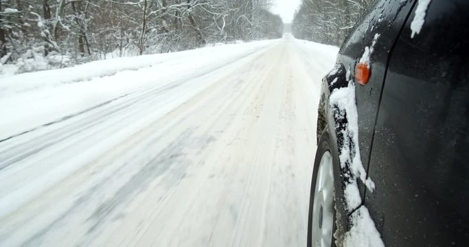 Color footage of a car driving on a snowy road, with close up on the wheel.