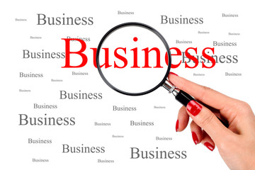 Woman with red nail polish holding a magnifying Glass over the word Business