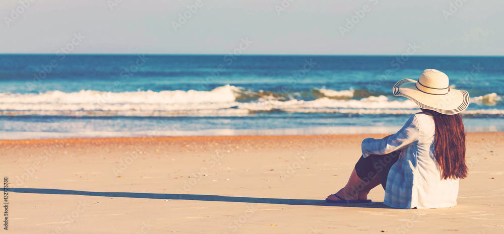 Wall mural woman in a hat sitting on the beach