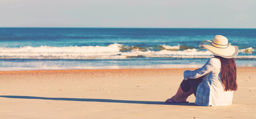 Fototapeta na wymiar Woman in a hat sitting on the beach