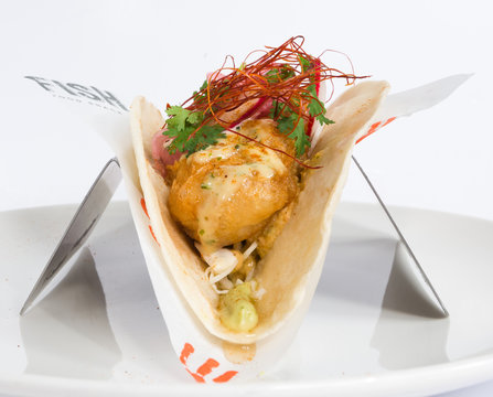 Golden Fried Cod Fish Taco Isolated On A White Background, Served With Parsley, Red Onion Hollandaise Sauce, Radish,  And A Fresh Wedge Of Lime.