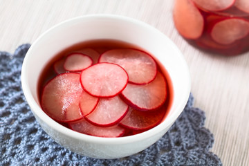 Fresh radishes cut in thin slices pickled in red wine vinegar with sugar and salt, photographed with natural light (Selective Focus, Focus on the front of the radish slice on the top)