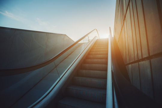 City Street Outdoor Grungy Modern Escalator Goes Up To Sun And Blue Sky, Rusty Metal Tiled Wall On The Right, View From The Rail, Barcelona, Spain