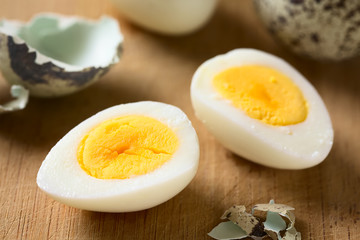 Hard boiled quail egg halves with egg shells on wooden board, photographed with natural light...