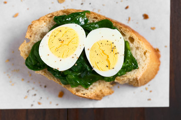 Crostini roasted bread slice with cooked spinach leaves and hard boiled quail eggs, photographed...