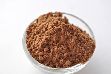 Raw cocoa (Theobroma cacao) powder in a glass bowl, closeup on white background

