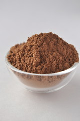 Raw cocoa (Theobroma cacao) powder in a glass bowl, closeup on white background
