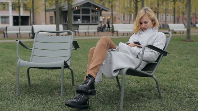 Girl With the Phone Sitting on a Chair in the Park
